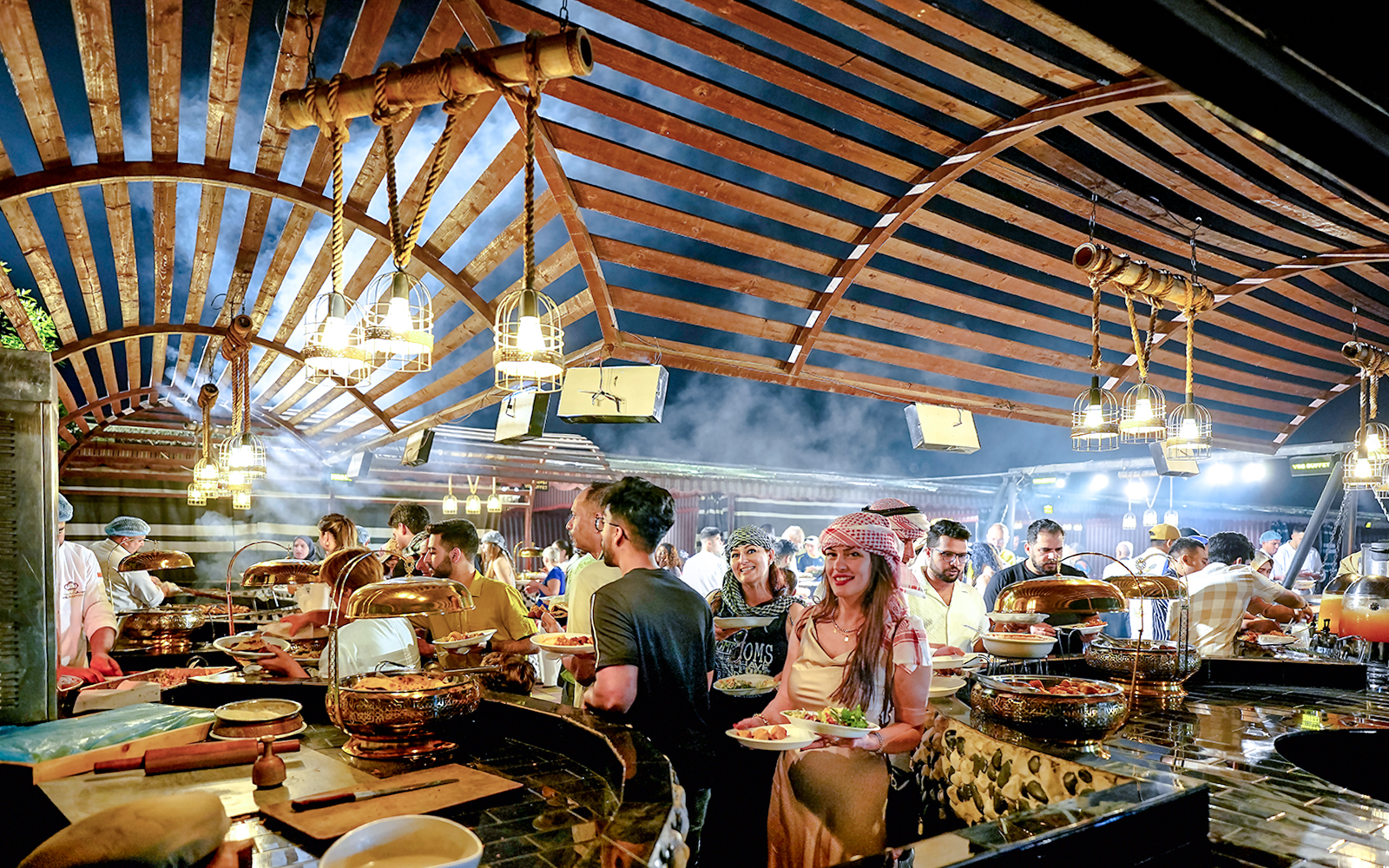 Guests enjoying buffet dinner under wooden canopy during evening desert safari.