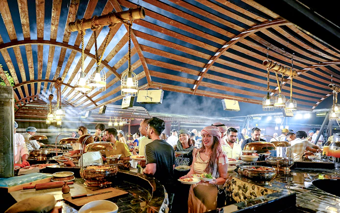 Guests enjoying buffet dinner under wooden canopy during evening desert safari.