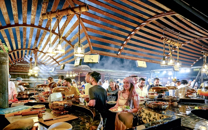Guests enjoying buffet dinner under wooden canopy during evening desert safari.