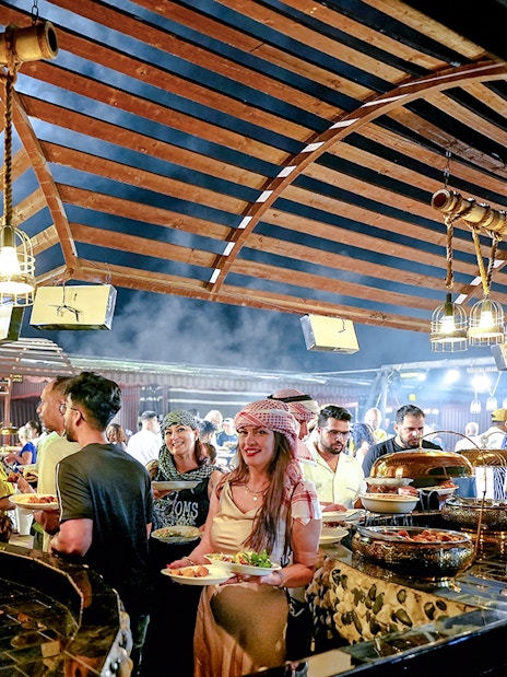 Guests enjoying buffet dinner under wooden canopy during evening desert safari.