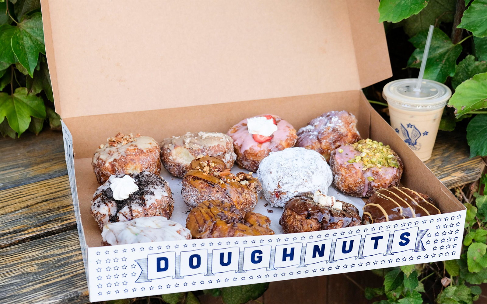 Box of assorted gourmet donuts with various toppings on a wooden table.
