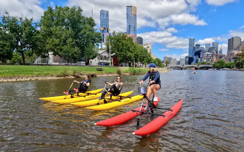 People riding waterbikes on the Yarra River with Melbourne skyline in the background.