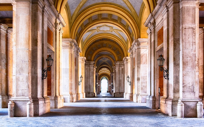 Royal Palace of Caserta interior with grand arched hallway and ornate columns.
