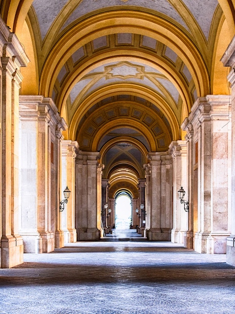 Royal Palace of Caserta interior with grand arched hallway and ornate columns.
