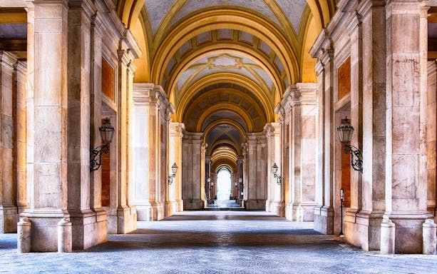 Royal Palace of Caserta interior with grand arched hallway and ornate columns.