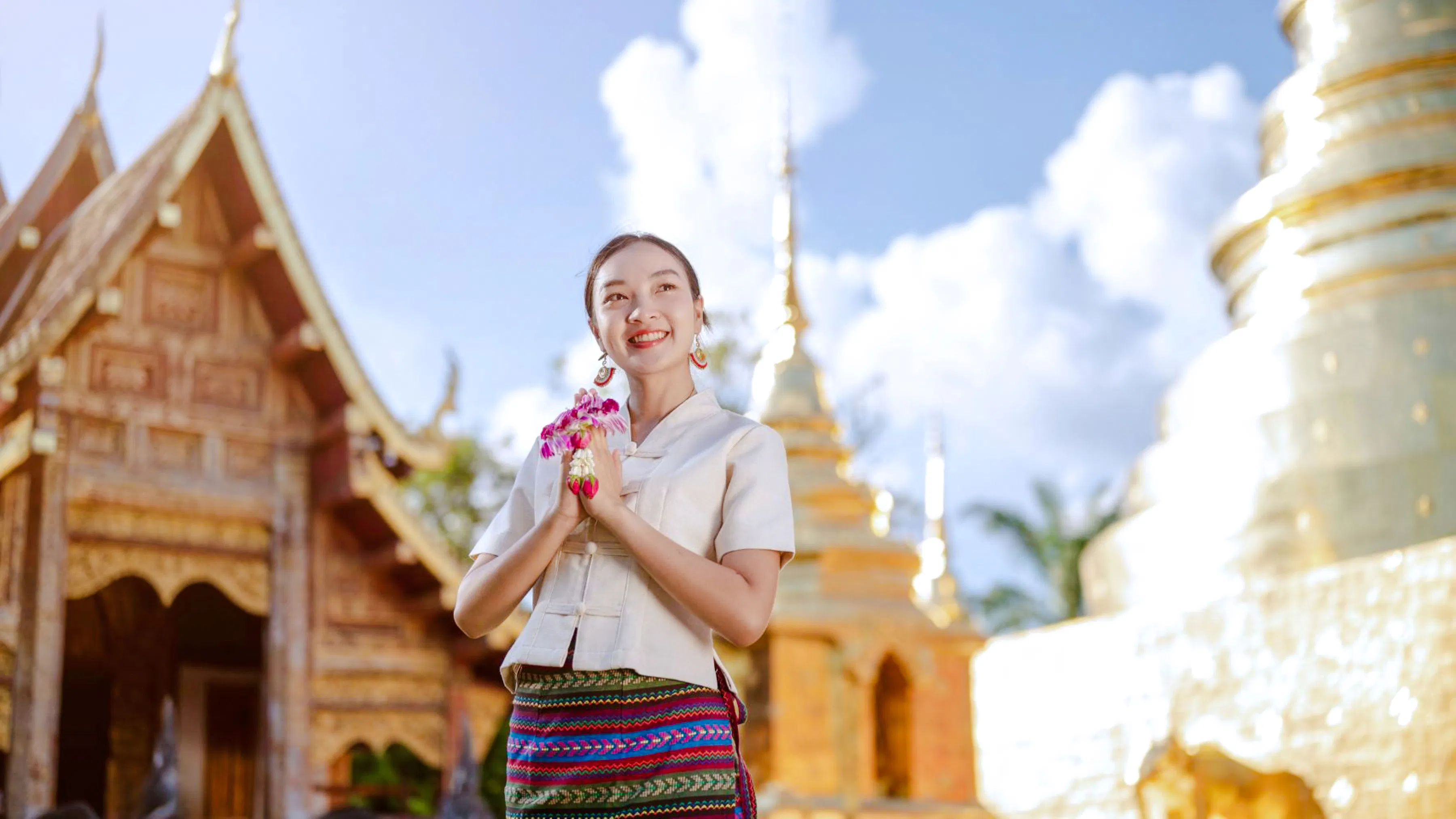 Person in traditional Thai attire at a temple in Chiang Mai, holding flowers.