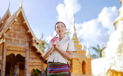 Person in traditional Thai attire at a temple in Chiang Mai, holding flowers.