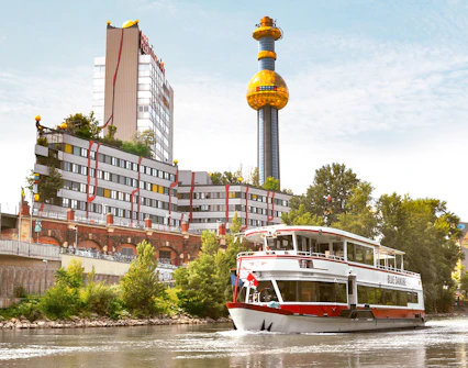 Sightseeing cruise boat on the Danube Canal passing the colorful Spittelau incinerator in Vienna.