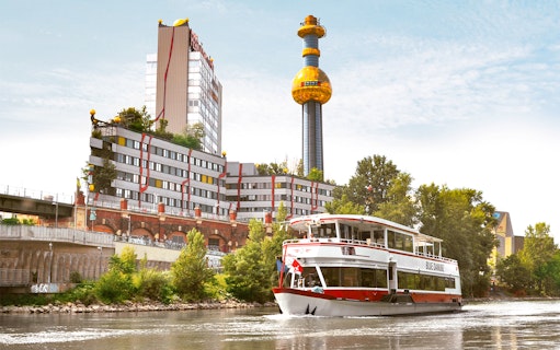 Sightseeing cruise boat on the Danube Canal passing the colorful Spittelau incinerator in Vienna.