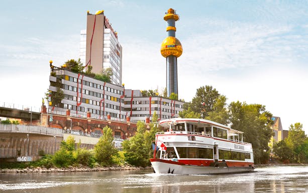Sightseeing cruise boat on the Danube Canal passing the colorful Spittelau incinerator in Vienna.
