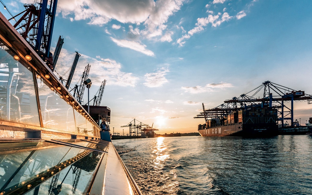 Harbor view with cranes and cargo ship at sunset in Hamburg, Germany.