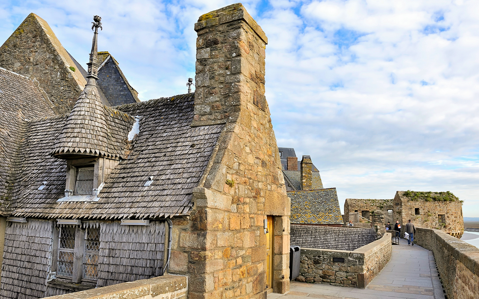 Remparts of Mont Saint Michel with stone buildings and walkway under a blue sky.