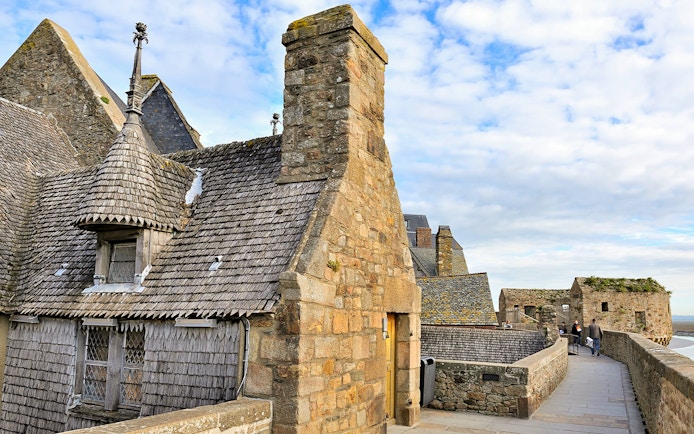 Remparts of Mont Saint Michel with stone buildings and walkway under a blue sky.
