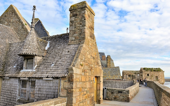 Remparts of Mont Saint Michel with stone buildings and walkway under a blue sky.