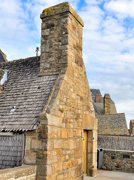 Remparts of Mont Saint Michel with stone buildings and walkway under a blue sky.