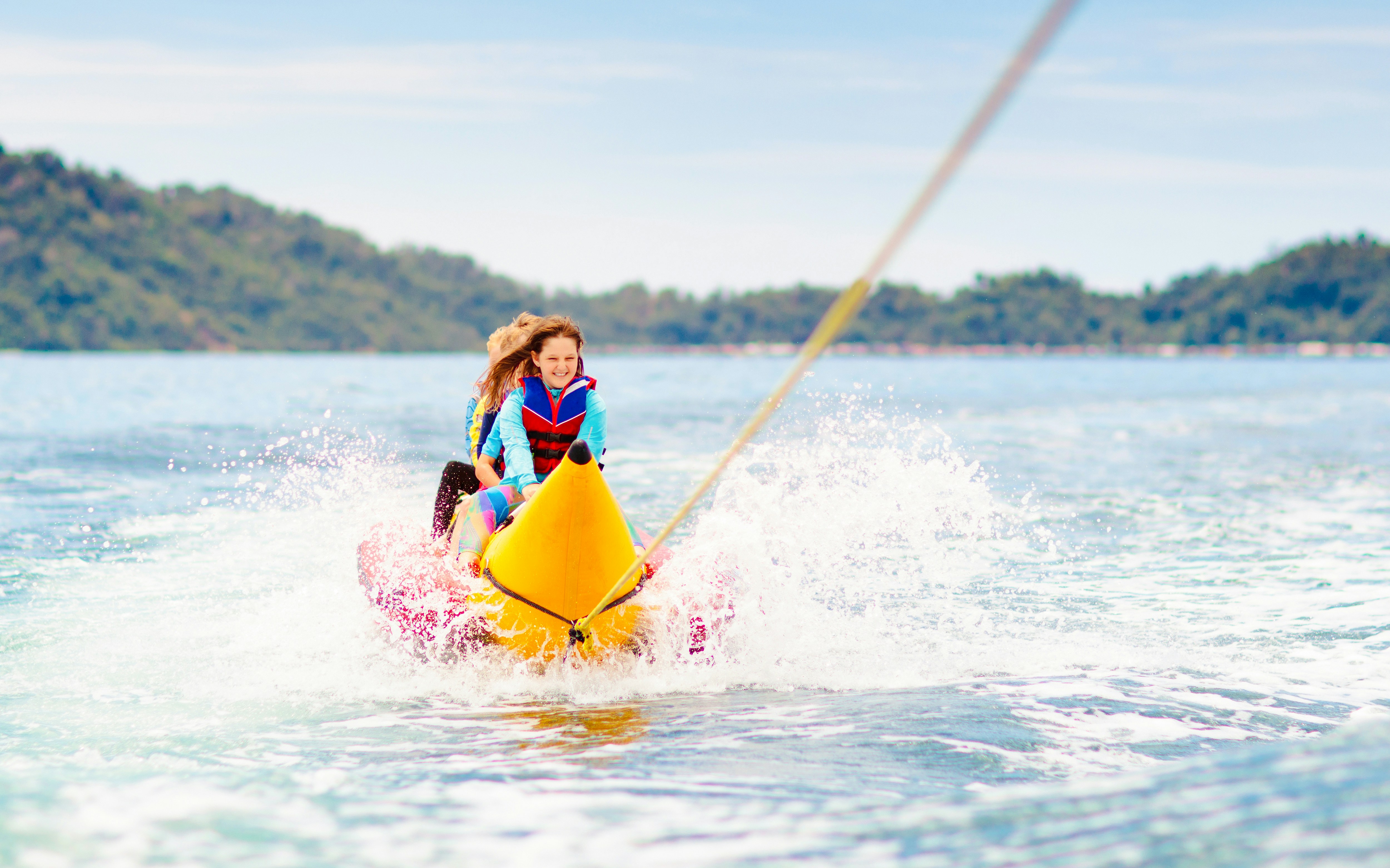 Kids enjoying a banana boat ride on the ocean with distant hills in the background.