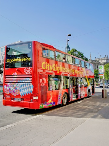 Red double-decker bus for city sightseeing in Munich, Germany, parked on a street.