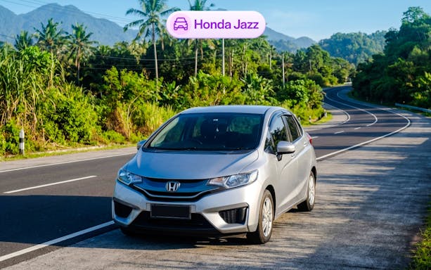 Honda Jazz parked on a scenic road in Bali with lush greenery and mountains.