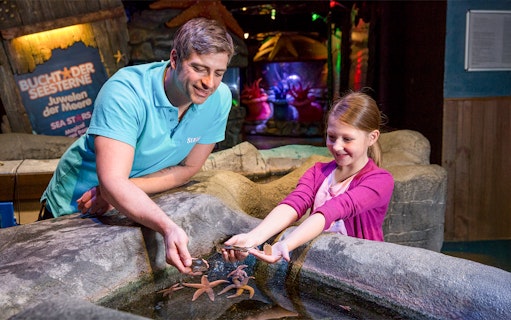 Sea Life staff guiding child at touch pool with starfish in Oberhausen.
