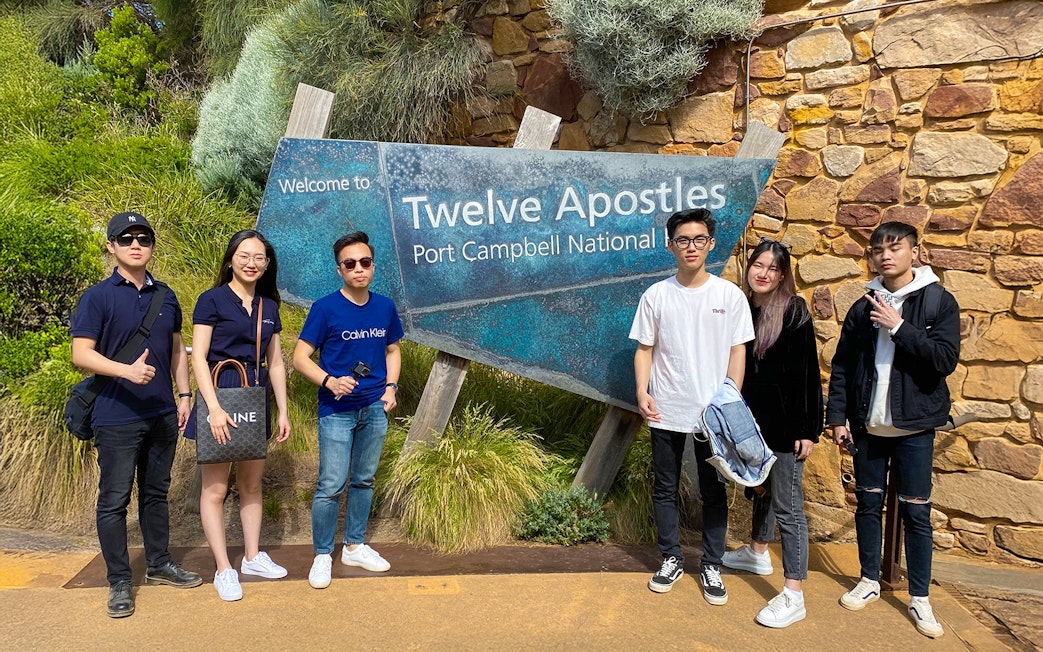 Group of people standing by Twelve Apostles sign on Great Ocean Road, Port Campbell National Park.