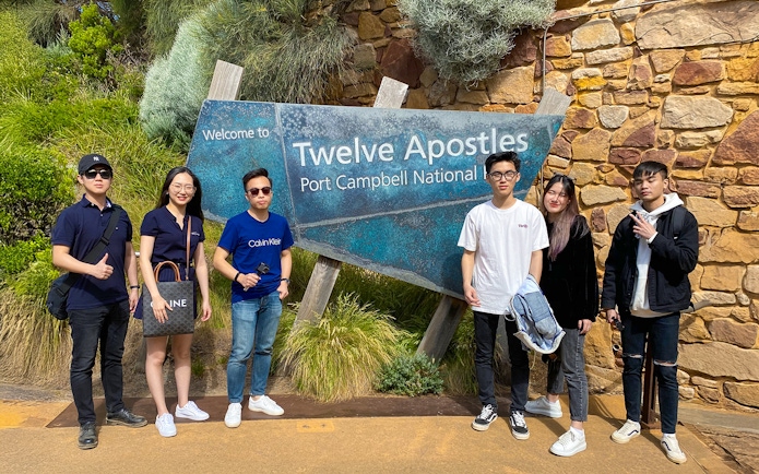 Group of people standing by Twelve Apostles sign on Great Ocean Road, Port Campbell National Park.