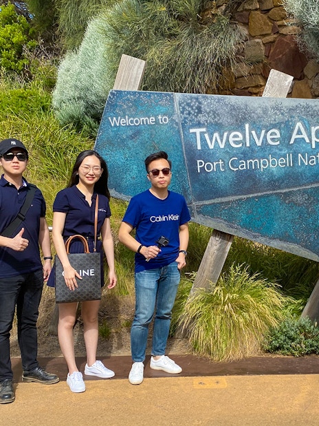 Group of people standing by Twelve Apostles sign on Great Ocean Road, Port Campbell National Park.