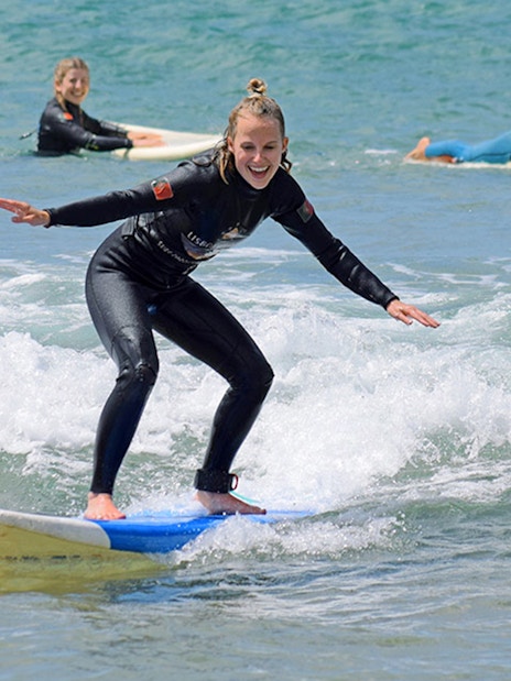 Group surf lesson participants riding waves in Lisbon.