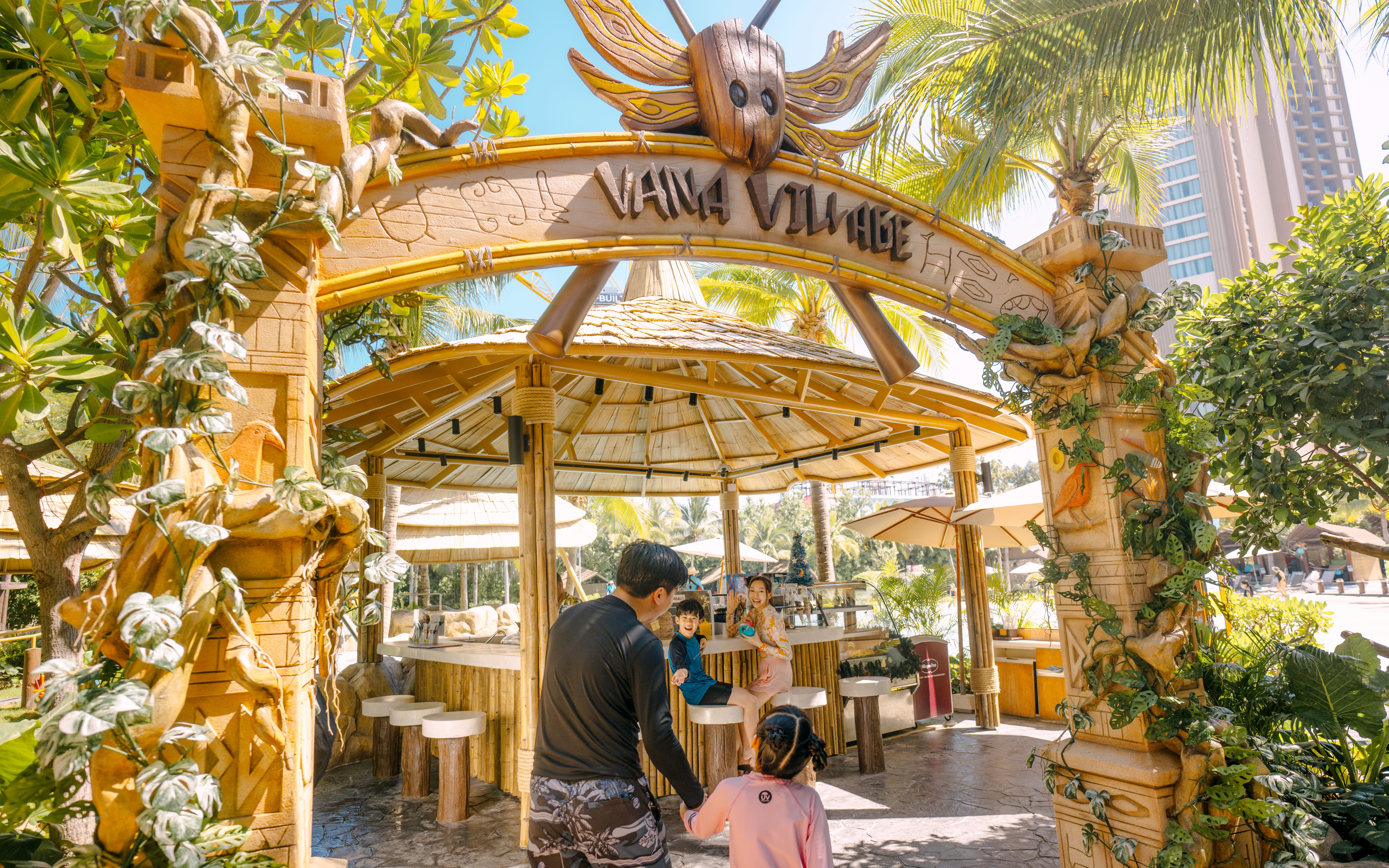 Family entering Vana Nava Water Jungle's Vana Village, surrounded by tropical decor and greenery.