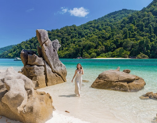 Surin Island beach with rock formations and a woman walking by the turquoise sea, Phuket day trip.