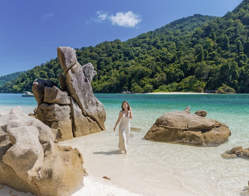 Surin Island beach with rock formations and a woman walking by the turquoise sea, Phuket day trip.
