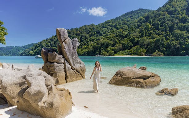 Surin Island beach with rock formations and a woman walking by the turquoise sea, Phuket day trip.