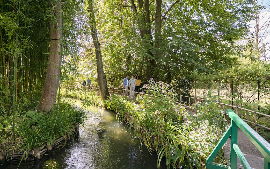 Visitors walking along a path in Giverny Gardens, surrounded by lush greenery and a small stream.