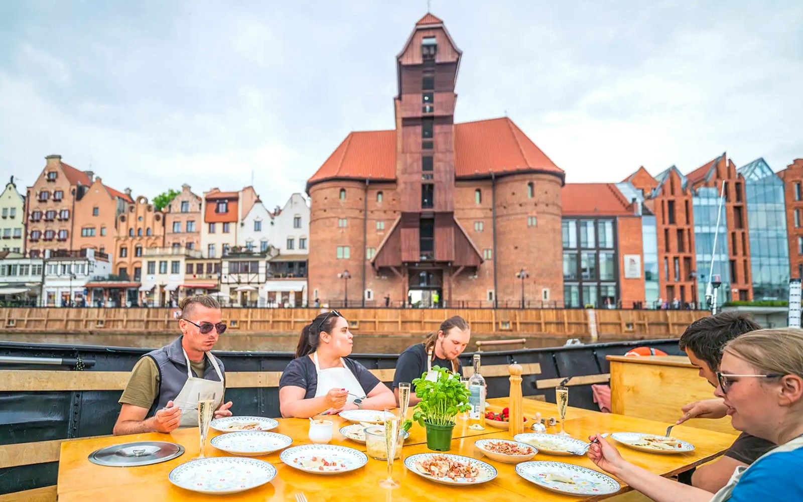 Guests tasting pierogi on Motława River Cruise in Gdansk with historic buildings in view.