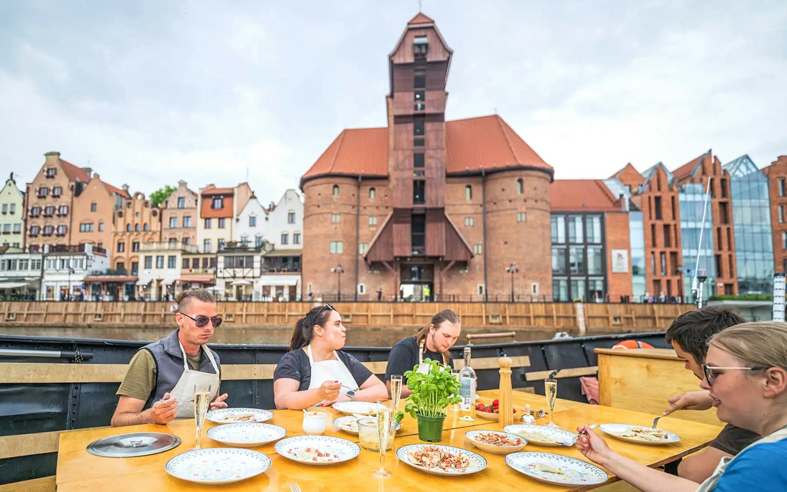 Guests tasting pierogi on Motława River Cruise in Gdansk with historic buildings in view.