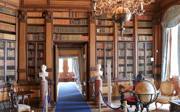 Miramare Castle reading room with bookshelves, busts, and a globe.