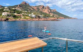 Paddleboarder near catamaran in Villefranche bay with coastal view.