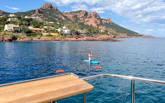 Paddleboarder near catamaran in Villefranche bay with coastal view.