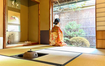 Person in kimono sitting in traditional Kyoto tea room, looking at garden.