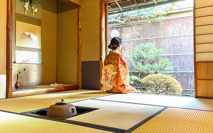 Person in kimono sitting in traditional Kyoto tea room, looking at garden.