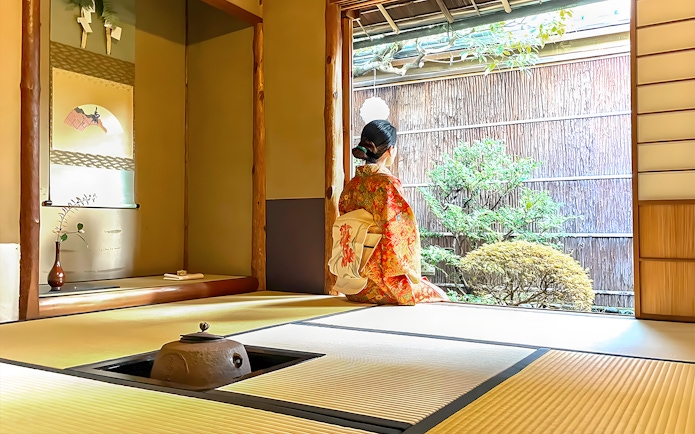 Person in kimono sitting in traditional Kyoto tea room, looking at garden.