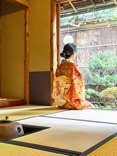 Person in kimono sitting in traditional Kyoto tea room, looking at garden.