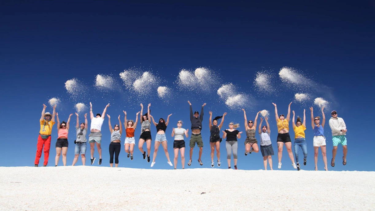 Group enjoying sandboarding adventure in Lancelin, Australia, throwing sand in the air.