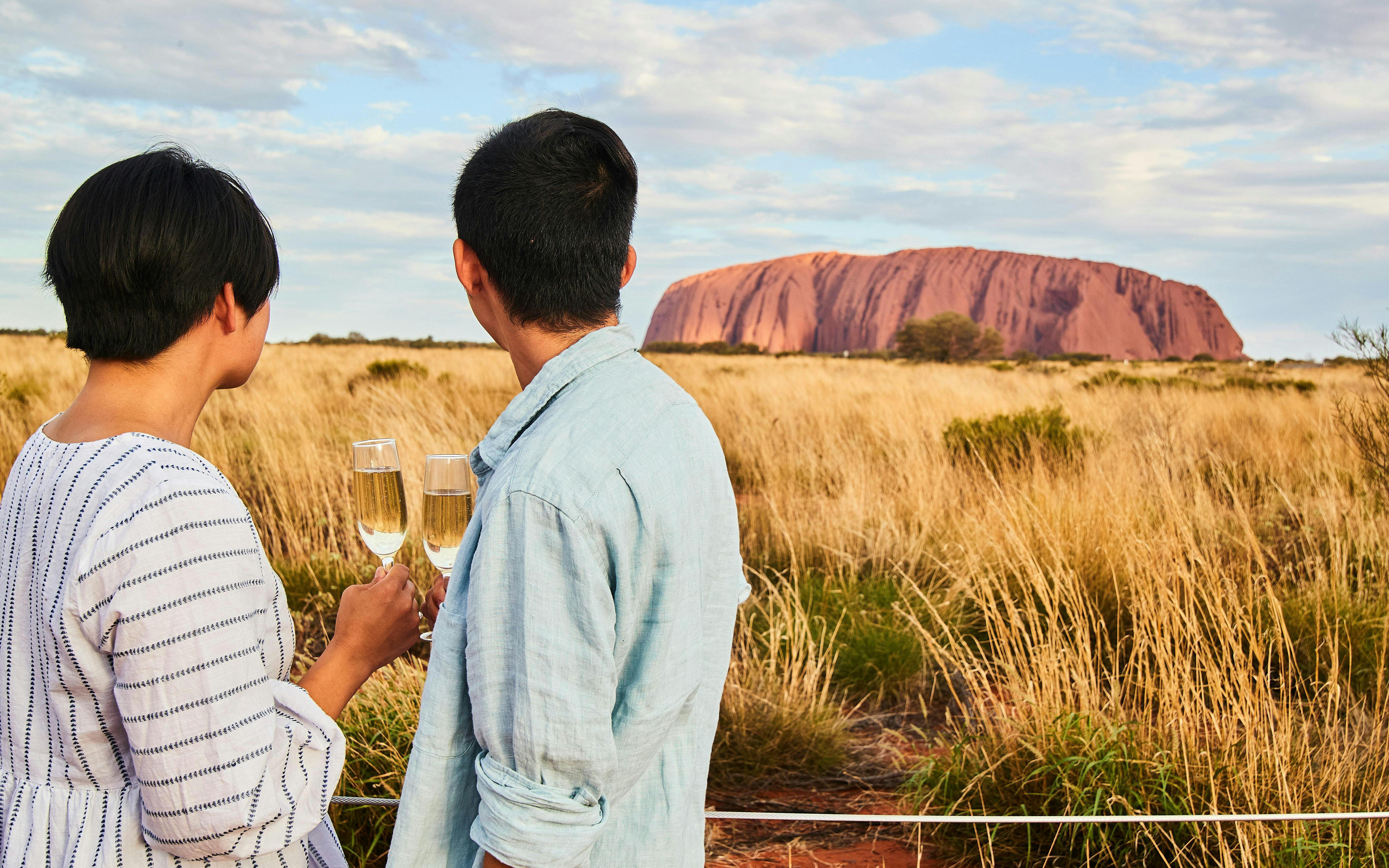 Couple enjoying sparkling wine with view of Uluru at sunset.