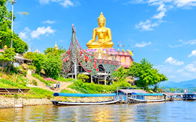 Golden Buddha statue at Golden Triangle, Chiang Rai, with boats on the Mekong River.