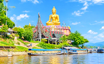 Golden Buddha statue at Golden Triangle, Chiang Rai, with boats on the Mekong River.