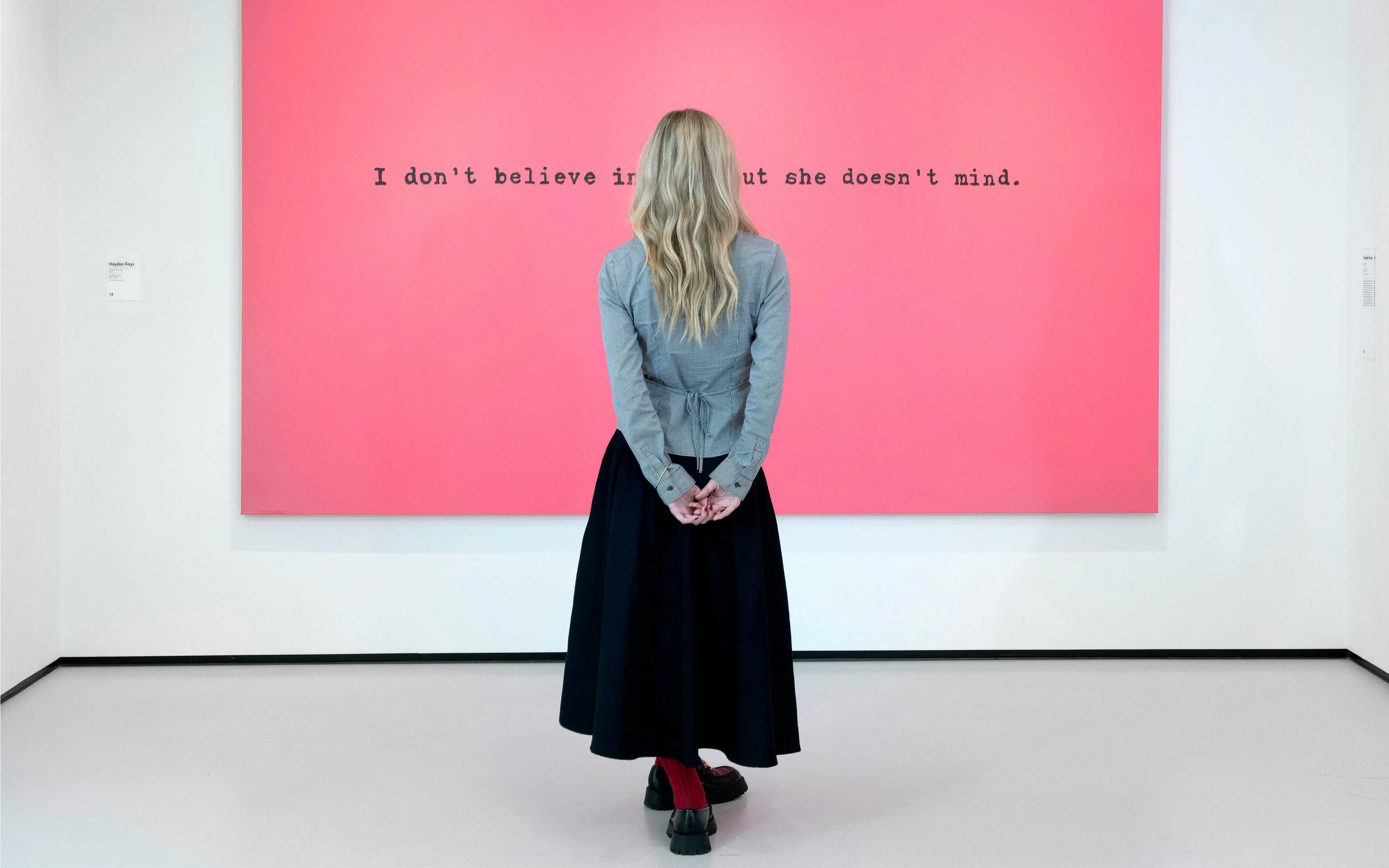 Visitor viewing pink artwork with text at Moco Museum, London.