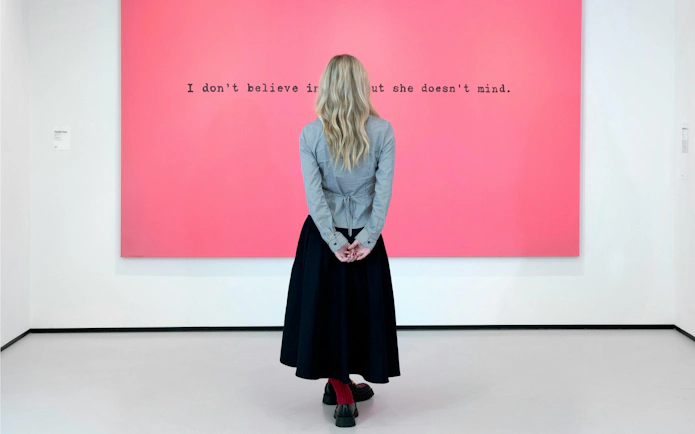 Visitor viewing pink artwork with text at Moco Museum, London.