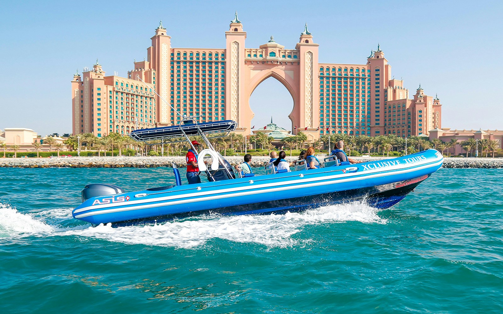 Speedboat cruising past Dubai Marina skyscrapers with Atlantis and Burj Al Arab in view.