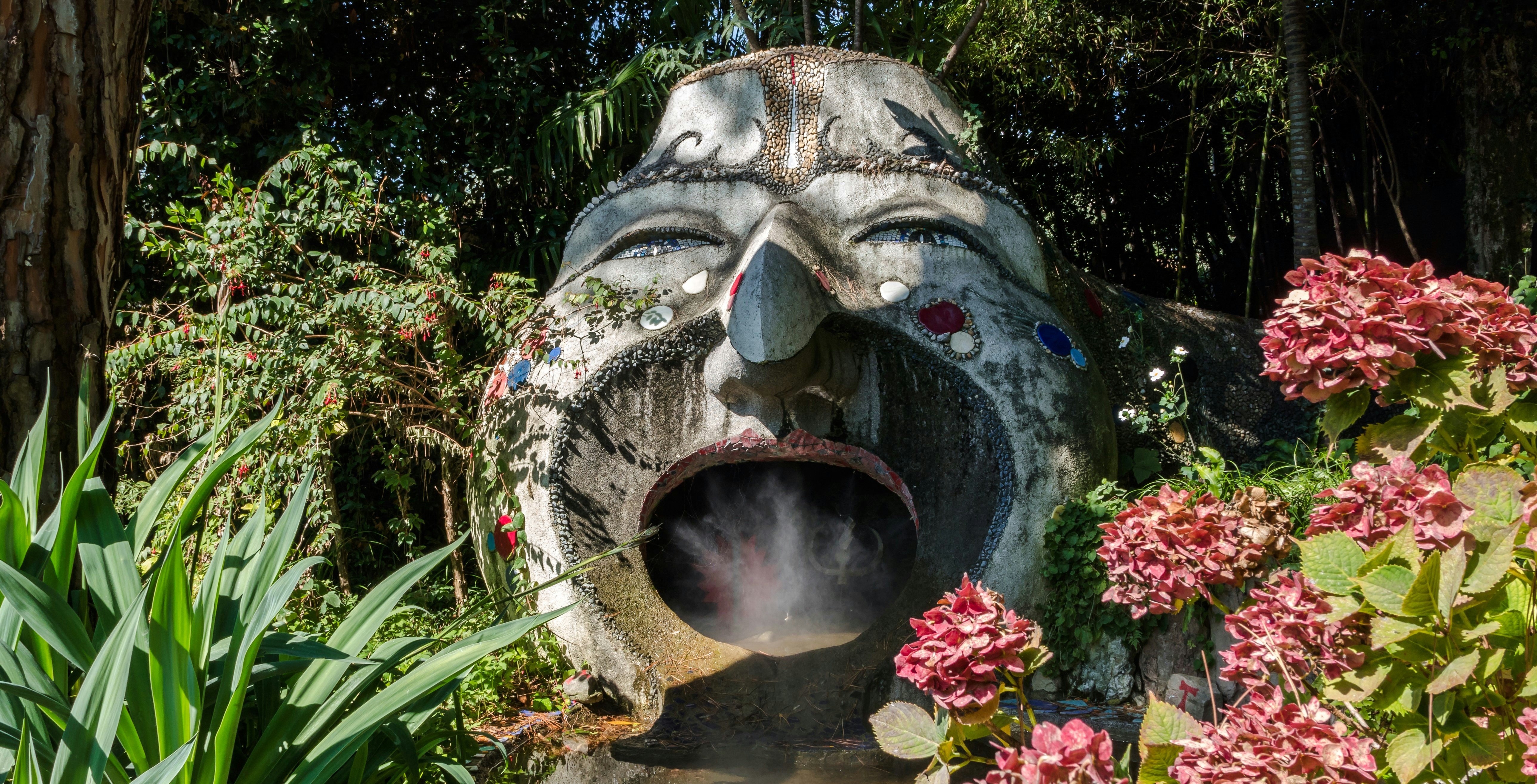 Stone sculpture with open mouth surrounded by lush plants at ANIMA Garden, Marrakech.