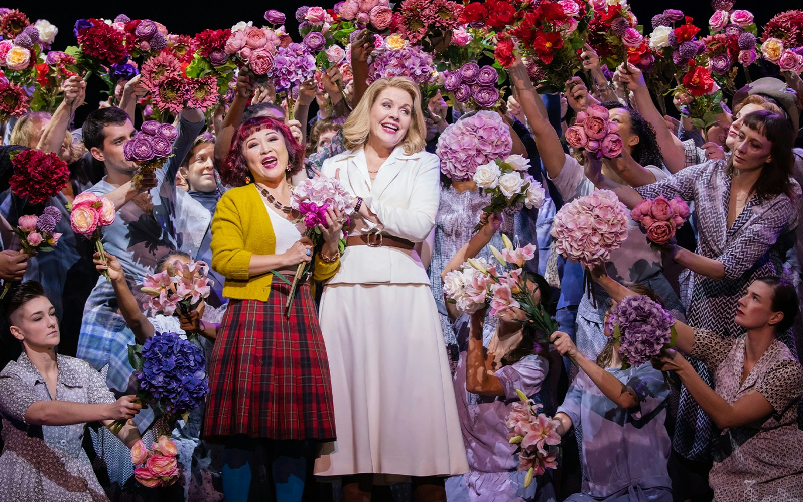 Performers holding colorful flowers during a scene from "The Hours" musical.